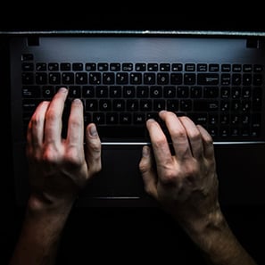 A closeup of hands typing at a keyboard in a dark room.