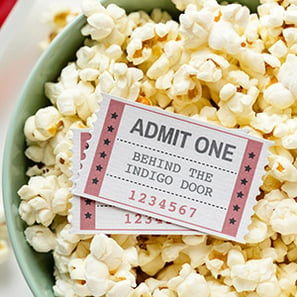 A cloeup of a bowl of popcorn with two movie tickets on top.