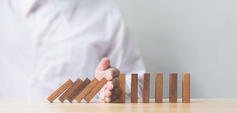 A hand stopping a row of dominoes from falling over