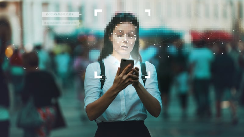 An image of a woman with a pixelated face, standing in a city street looking at her phone.