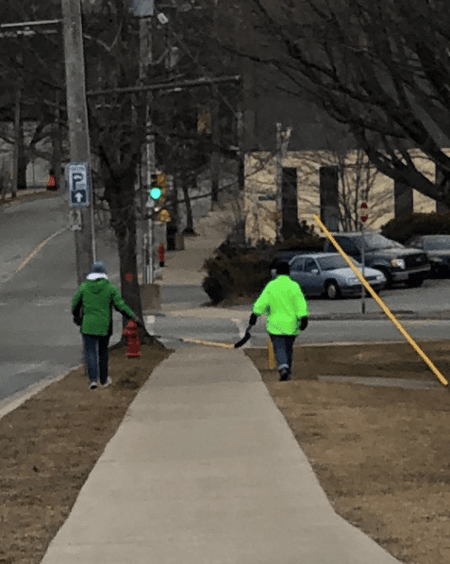Two people walking socially distant, using a hockey stick to measure 6 feet between them.