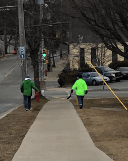 Two people walking socially distant, using a hockey stick to measure 6 feet between them.